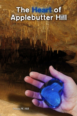 The Heart of Applebutter Hill book cover shows cave scene: stalactites reflected in an underground lake, while a hand holds the Heartstone of Arden-Goth, a blue, heart-shaped sapphire