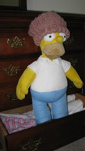 Homer Simpson doll is standing in lower dresser drawer wearing winter hat, knitted in Lynda Lambert's pattern by Donna W. Hill using Caron’s Simply Soft Victorian Rose yarn: Homer, courtesy of Mary McAleavey; photo by Rich Hill.