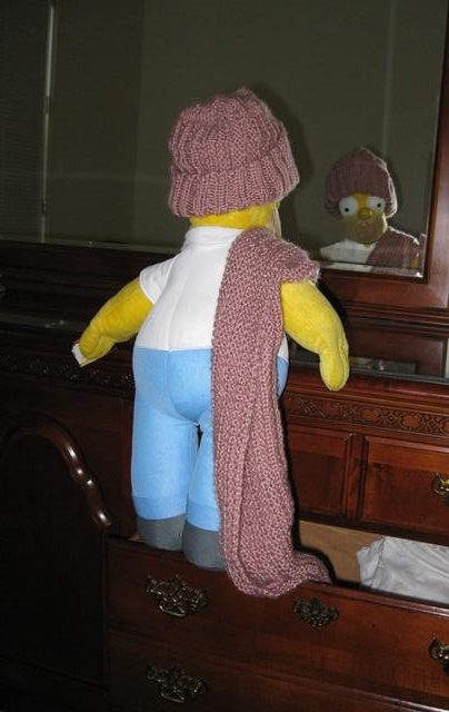 The Homer Simpson doll has climbed up the dresser. He’s admiring himself in the mirror, wearing a winter hat. The matching scarf – knitted in Lynda’s one-row pattern by Donna W. Hill, using Caron’s Simply Soft Victorian Rose yarn - is over his right shoulder, and he’s pulling it from the drawer : Homer, courtesy of Mary McAleavey; photo by Rich Hill.